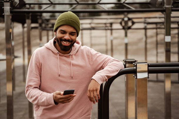alegre afroamericano hombre en ropa deportiva charlando en el teléfono celular en el campo de deportes - Foto, Imagen