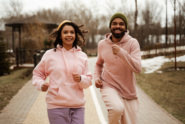 cheerful african american joggers looking at camera while running outdoors - Photo, Image