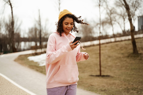 junge afrikanisch-amerikanische Joggerin hält Handy beim Laufen im Freien - Foto, Bild