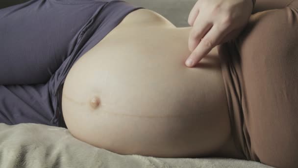 mujer embarazada acostada en el sofá, jugando con el vientre, pisándola con los dedos - Imágenes, Vídeo