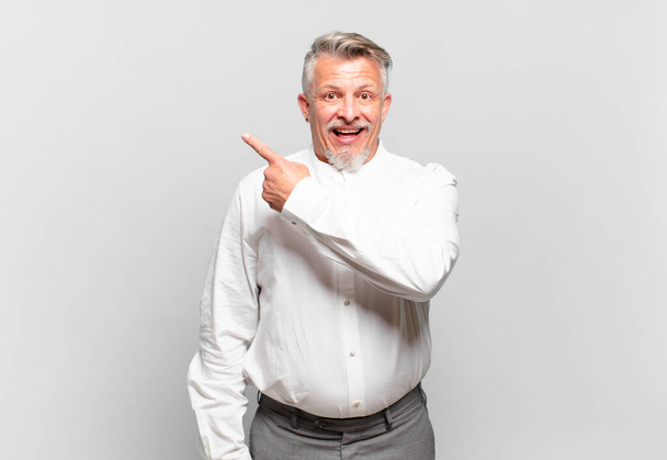 senior businessman looking excited and surprised pointing to the side and upwards to copy space - Foto, Bild