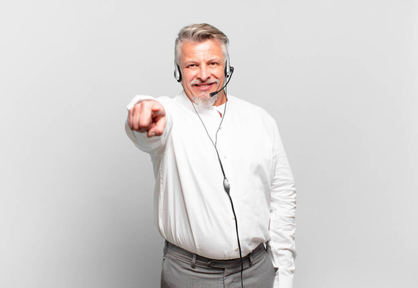 senior telemarketer pointing at camera with a satisfied, confident, friendly smile, choosing you - Fotoğraf, Görsel
