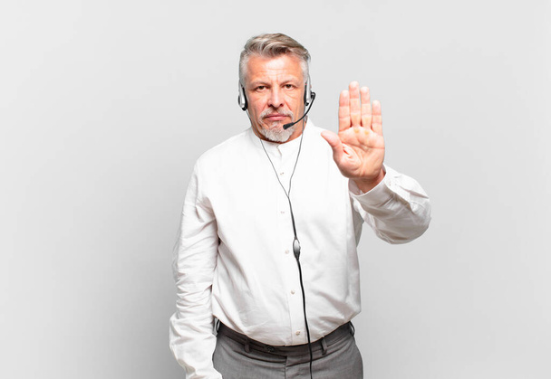 senior telemarketer looking serious, stern, displeased and angry showing open palm making stop gesture - Valokuva, kuva