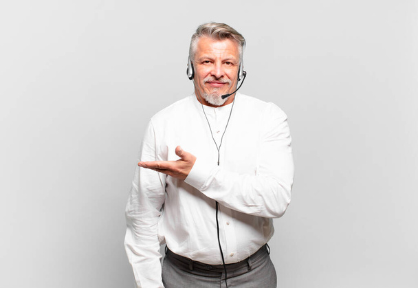 senior telemarketer smiling cheerfully, feeling happy and showing a concept in copy space with palm of hand - Fotografie, Obrázek