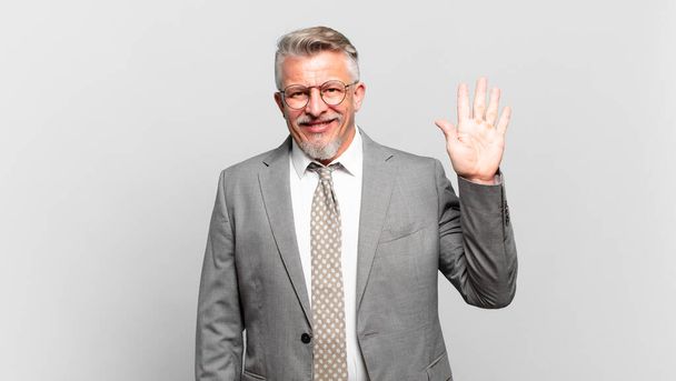 senior businessman smiling happily and cheerfully, waving hand, welcoming and greeting you, or saying goodbye - Valokuva, kuva