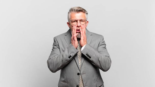 senior businessman feeling shocked and scared, looking terrified with open mouth and hands on cheeks - Fotografie, Obrázek