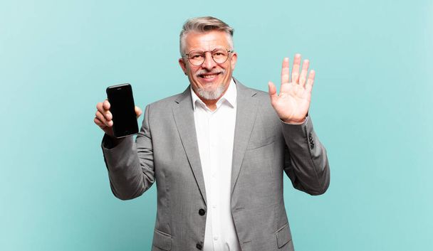 senior businessman smiling happily and cheerfully, waving hand, welcoming and greeting you, or saying goodbye - Foto, afbeelding