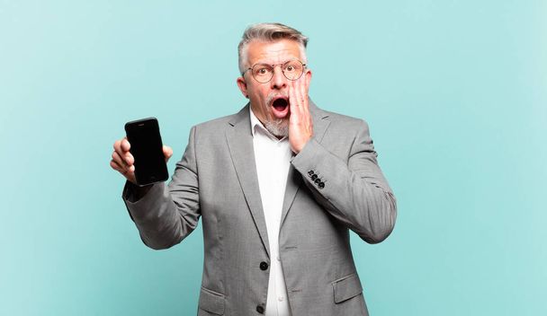 senior businessman feeling shocked and scared, looking terrified with open mouth and hands on cheeks - 写真・画像