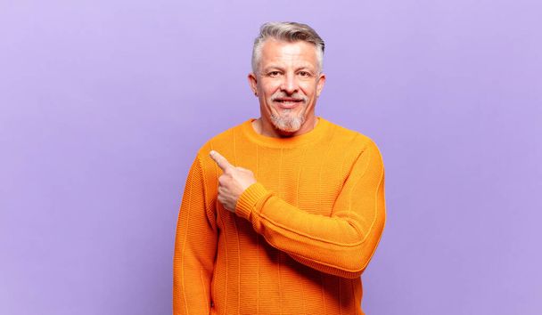 old senior man smiling cheerfully, feeling happy and pointing to the side and upwards, showing object in copy space - Photo, image