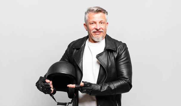 senior motorbike rider smiling cheerfully, feeling happy and showing a concept in copy space with palm of hand - Фото, зображення