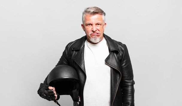 senior motorbike rider looking puzzled and confused, biting lip with a nervous gesture, not knowing the answer to the problem - 写真・画像
