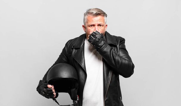 senior motorbike rider covering mouth with hands with a shocked, surprised expression, keeping a secret or saying oops - 写真・画像