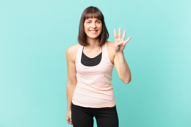 athlete woman smiling and looking friendly, showing number four or fourth with hand forward, counting down - Foto, afbeelding