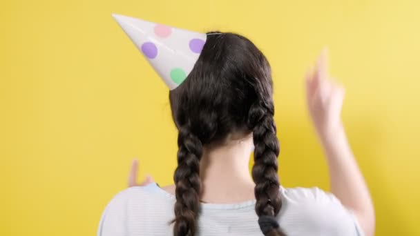 A woman in the paper cap is having fun, and then turns around and looks sad, showing a protective mask. Yellow background. The concept of celebrating during the coronavirus pandemic - Footage, Video