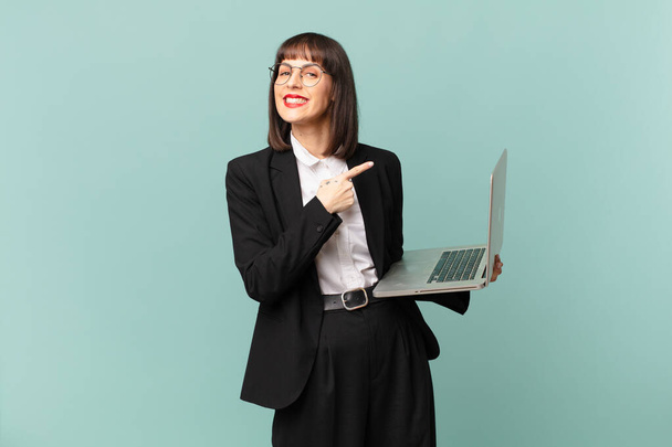 businesswoman smiling cheerfully, feeling happy and pointing to the side and upwards, showing object in copy space - Foto, Imagen