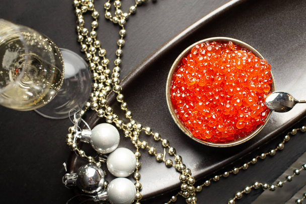 Red caviar in a a ceramic bowl, silver beads and pearlsand a glass of champagne on a silver tray. Christmas and New Year background - Photo, Image