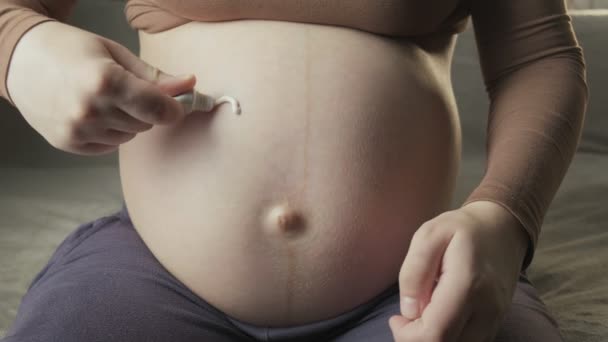 Mujer embarazada dibujando el símbolo del corazón con crema blanca para el cuidado de la piel en su vientre - Imágenes, Vídeo