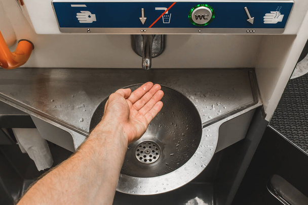 The guy brings his hand to the automatic water supply tap in the modern toilet of the stadler electric train. - Photo, Image