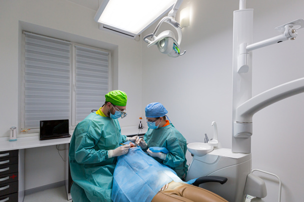 Team of dental surgeons performs surgery on teeth. in a modern clinic. Young dentist. Teamwork. Tooth doctor orthodontist surgeon doing medical operation on root canals. Stomatology office. - Foto, afbeelding