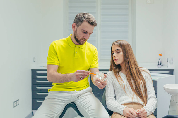 A male dentist explains and teaches a female patient how to brush her teeth properly, after dental procedures, at her dental clinic - Foto, imagen