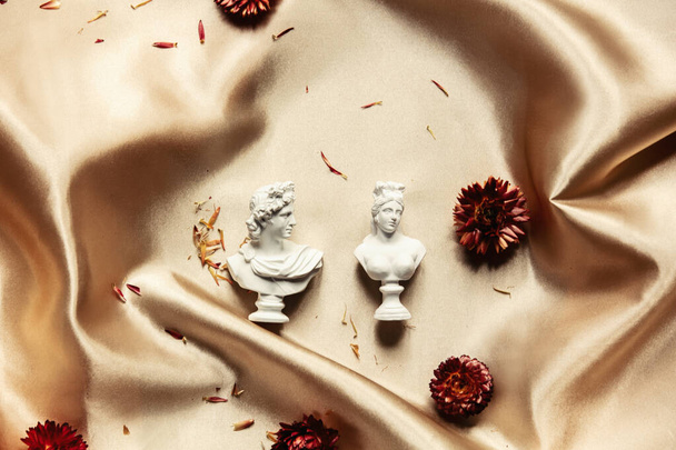 Male and females busts with flower heads around on golden fabric. Top view  - Photo, Image