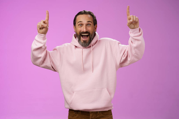 Energized happy good-looking trendy mature dad beard grey hair in pink stylish capodie wearing son outfit pointing up index fingers thrilled favorite music group in town, standing purple background - Fotografie, Obrázek