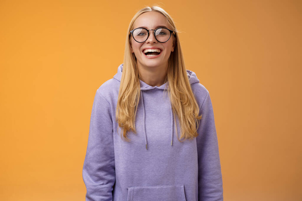 Karizmatikus vidám bájos mosolygós női egyetem egyenes a tanuló szemüvegben lila hangulatos kapucnis vigyorgás nevetés boldogan boldog meghívott kéz ki osztálytársak álló narancs háttér - Fotó, kép