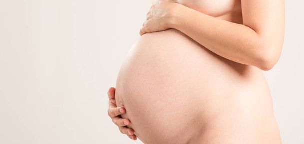 Roztomilé těhotné břicho izolované na bílém. Pohled z boku mladé těhotné ženy objímající své nahé břicho rukama. Koncept žena těhotný život - Fotografie, Obrázek