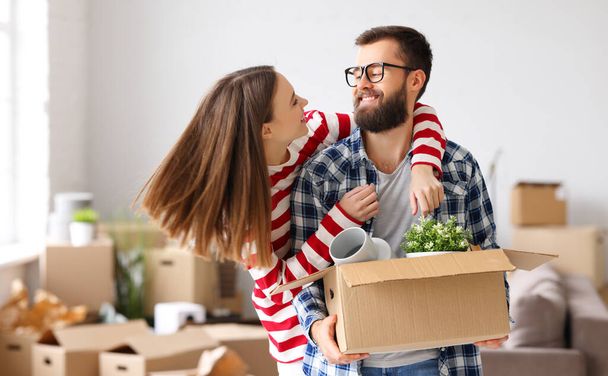 Mujer encantada abrazando sonriente hombre de pie con caja de cartón en nuevo apartamento durante la reubicación y mirándose entre sí - Foto, Imagen