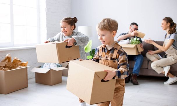 Cheerful kids helping parents with carrying stuff in carton boxes during moving in new apartment - Photo, Image