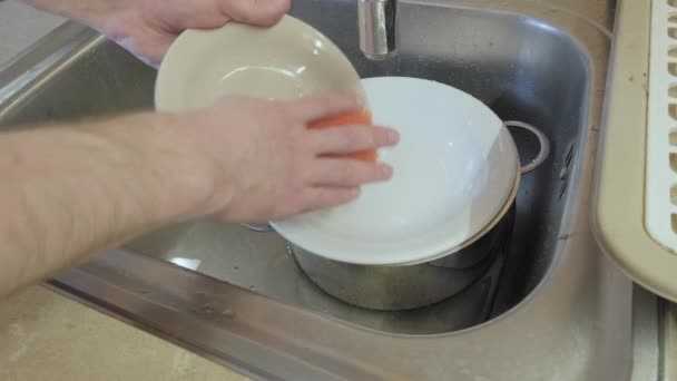 Человек моет посуду в железной раковине. Он аккуратно вытирает тарелки губкой. - Кадры, видео