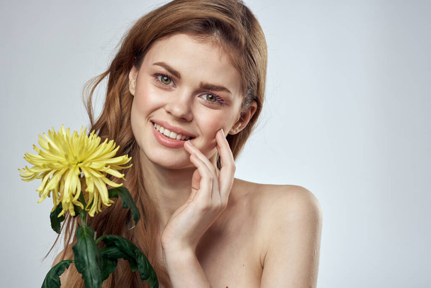 Portrait of a beautiful woman with a yellow flower on a light background cropped with Copy Space Model - Photo, Image