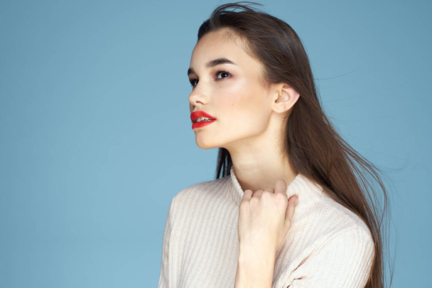 Brunette in een witte trui rode lippen charme lang haar blauwe achtergrond - Foto, afbeelding