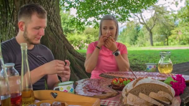 Uomo e donna mangiano salumi e formaggi da tagliere all'aperto - Filmati, video