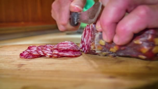 Dłonie trzymają salami podczas krojenia na drewnianej desce do krojenia - Materiał filmowy, wideo