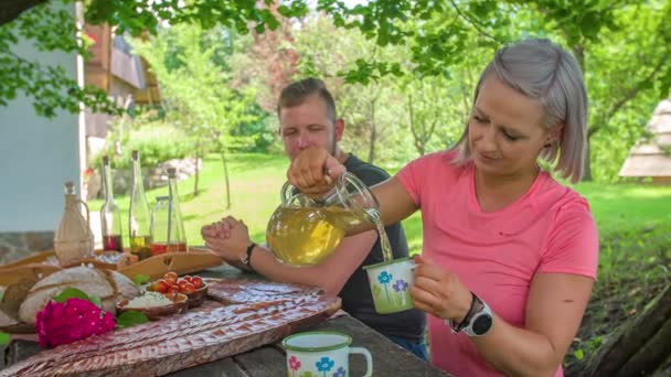 Donna al tavolo da picnic versa bevanda per l'uomo per andare con pasto gourmet - Filmati, video