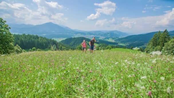 Giovane coppia escursionista trekking nella valle dei fiori circondata da splendide montagne. Al rallentatore. Angolo basso. Vista frontale. - Filmati, video