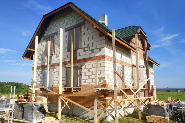 Μόνωση του σπιτιού με τούβλα πρόσοψης, κατασκευή ενός νέου σπιτιού και σκαλωσιές κοντά στους τοίχους.νέα - Φωτογραφία, εικόνα