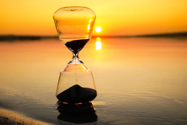 Stylish hourglass near river at sunset - Photo, Image