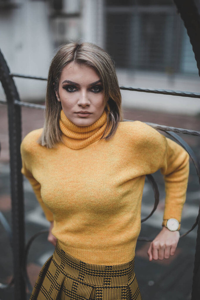 A young Caucasian female with a serious face from Bosnia Herzegovina in a yellow shirt posing outdoors - Foto, afbeelding