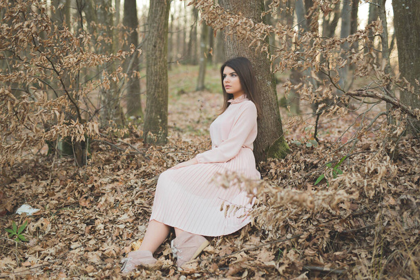 A young caucasian woman in an elegant pink dress sitting on the ground in a forest - Foto, Bild