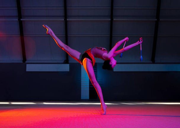 Joven gimnasta rítmica femenina aislada sobre fondo multicolor en luz de neón - Foto, Imagen