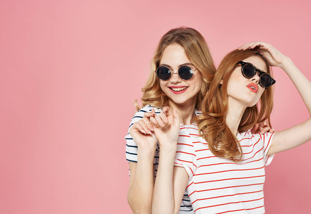 twee volwassen vrouwen dragen zonnebril communicatie vriendschap emoties vreugde roze achtergrond - Foto, afbeelding