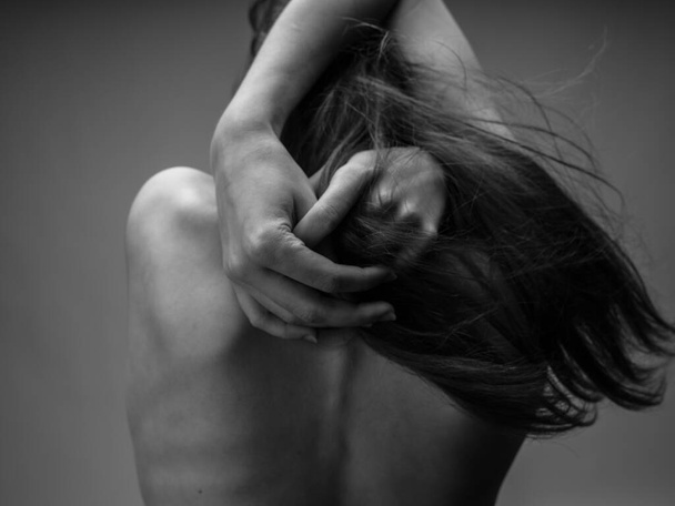 Kobieta na szarym zdjęciu dotyka się gołymi plecami. - Zdjęcie, obraz
