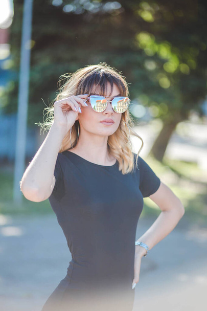 An attractive Caucasian woman from Bosnia Herzegovina in a black dress and sunglasses posing in a park - Фото, изображение