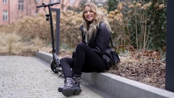 Happy kobieta z skuterem elektrycznym odpoczynku w jesiennym parku - Materiał filmowy, wideo