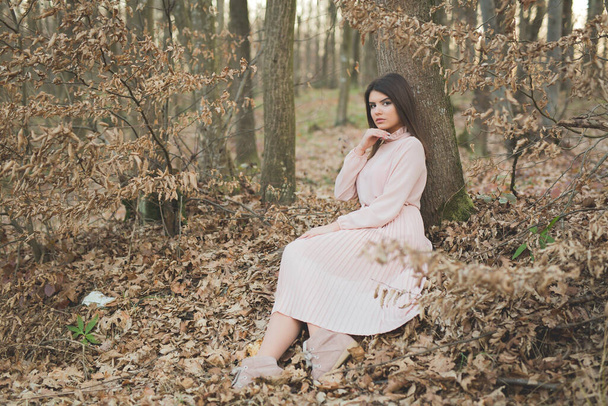 A young caucasian woman in an elegant pink dress sitting on the ground in a forest - Foto, afbeelding