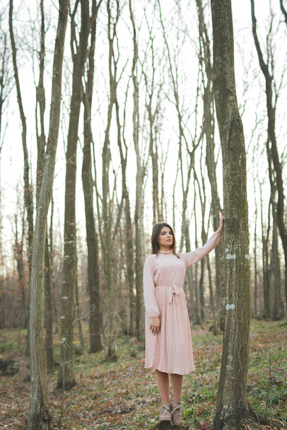 A vertical shot of a young caucasian woman in an elegant pink dress in a forest - Foto, Bild