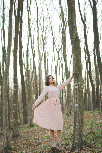 A young caucasian female in a delicate pink dress posing in a forest - Foto, Imagen