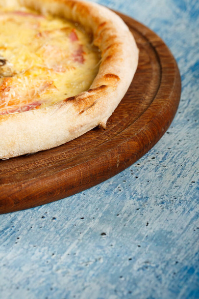 Pizza with a crispy crust on a wooden dance on a blue textured background. - Photo, Image